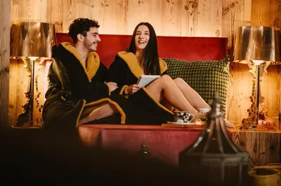 a man and a woman sitting on a couch with a tablet at Alpin Garden Luxury Maison & SPA - Adults Retreat in Ortisei