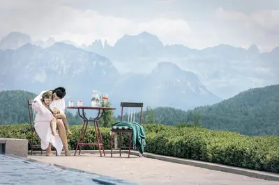 a bride and groom sitting at a table with mountains in the background at Parkhotel Holzner in Soprabolzano