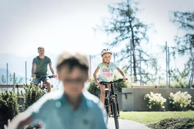 two people riding bikes down a sidewalk with a man at Parkhotel Holzner in Soprabolzano