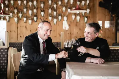 two men sitting at a table with glasses of wine at Hotel Ladinia in La Villa