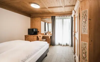 a bedroom with a bed and a desk and a television at Hotel Ladinia in La Villa