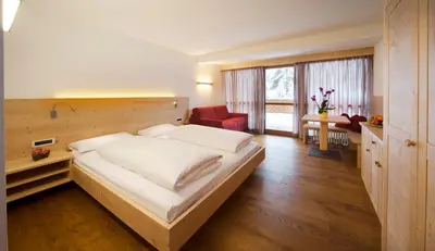 a bedroom with a large bed and a red chair at Hotel Ladinia in La Villa