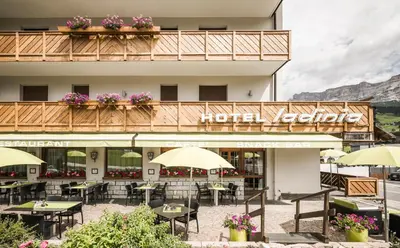 a hotel with tables and umbrellas in front of a building at Hotel Ladinia in La Villa