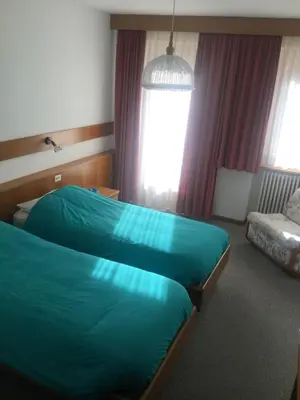 two beds in a hotel room with red sheets at Hotel Alpenrose in Alleghe