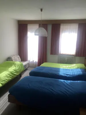 a hotel room with two beds and a chair at Hotel Alpenrose in Alleghe