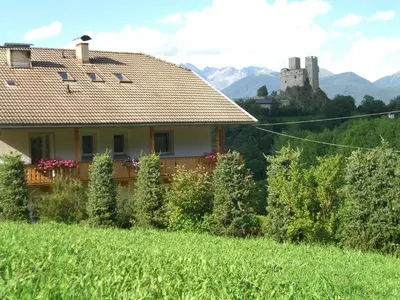 a house in a field with a castle in the background at Gutshof Erschbaumer in San Lorenzo di Sebato