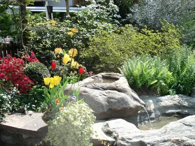 a garden with flowers and a pond and rocks at Hotel Sittnerhof in Merano
