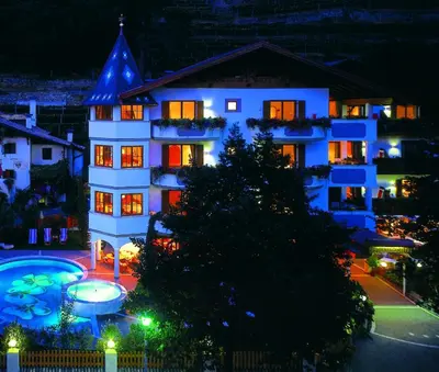a building with a lit up pool in front of it at night at Hotel Sittnerhof in Merano