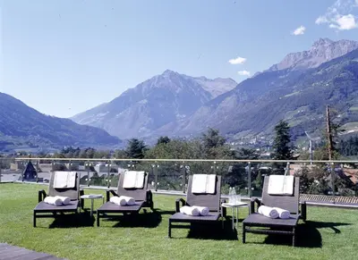 a group of chairs sitting in the grass with mountains in the background at Hotel Sittnerhof in Merano