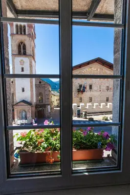 a window with a view of a church and flowers at Romantic Hotel Excelsior in Cavalese