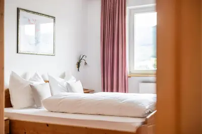 a bedroom with a bed with white pillows and a window at EGGER Apartments & Suites in Villandro