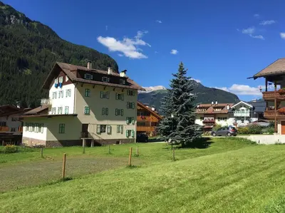 a large white house in a field with a tree at Central Apartment Canazei in Canazei