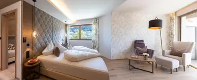 a bedroom with a bed and a chair and a table at Hotel Sonnbichl in Tirolo