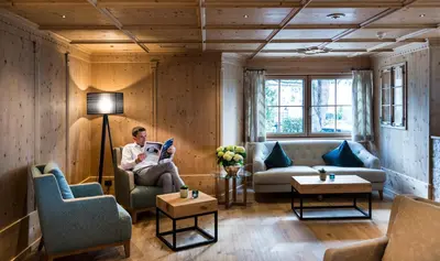 a man sitting in a chair in a living room at Hotel Sonnbichl in Tirolo