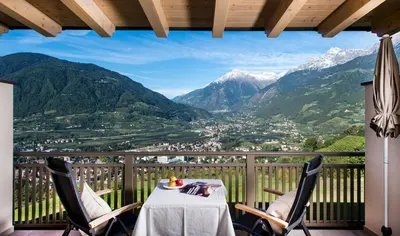 a table and chairs on a balcony with mountains at Hotel Sonnbichl in Tirolo