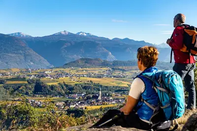 two people sitting on top of a mountain looking at a town at Strahlerhof in Appiano sulla Strada del Vino