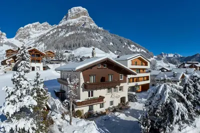 a house in the snow in front of a mountain at Alpin Relais B&B Villa Melisse in Colfosco