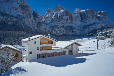 a house in the snow with mountains in the background at Alpin Relais B&B Villa Melisse in Colfosco