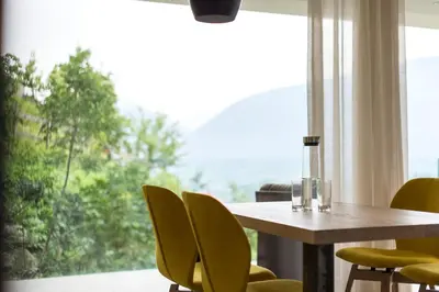 a dining room table with yellow chairs and a large window at Art & Nature Chalet Anna in Schenna