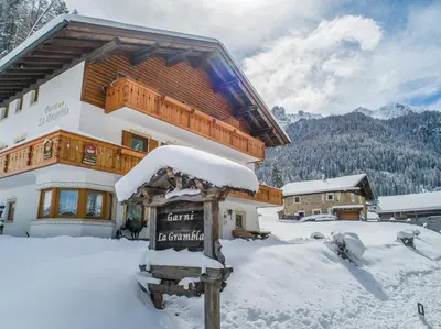 a snow covered building with a sign in front of it at Garnì La Grambla in Selva di Val Gardena