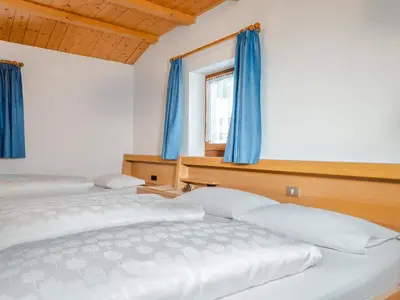 two beds in a bedroom with blue curtains at Garnì La Grambla in Selva di Val Gardena