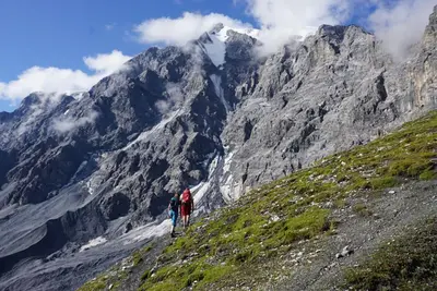 two people walking up a mountain with a snow covered mountain at Apartments Frieda in Valdaora