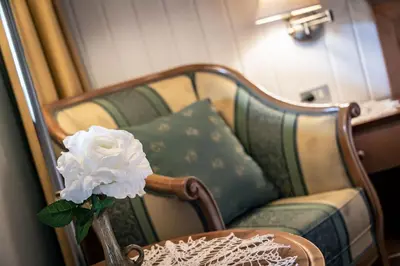 a white flower in a vase on a table next to a chair at Hotel Weisse Lilie - B&B in Mühlbach