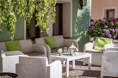 a patio with wicker chairs and a white table with green pillows at Hotel Weisse Lilie - B&B in Mühlbach