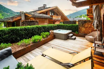 a deck with a hot tub and chairs on a house at Hotel Montchalet in Ortisei