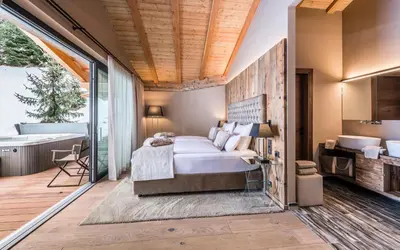 a bedroom with a bed and a bath room with a tub at Hotel Montchalet in Ortisei
