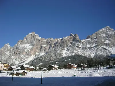a snow covered mountain with houses in front of it at Dolomiti Sport Hotel in San Vito di Cadore
