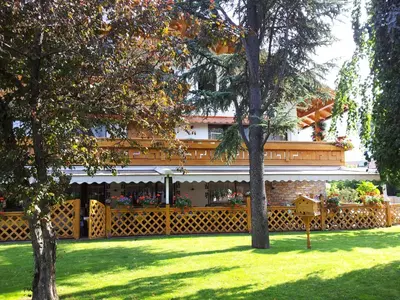 a building with a fence in a yard with trees at Hotel Hubertushof in Vipiteno