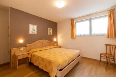 a bedroom with a bed and a desk and a window at Appartamenti Le Plejadi in Cavalese