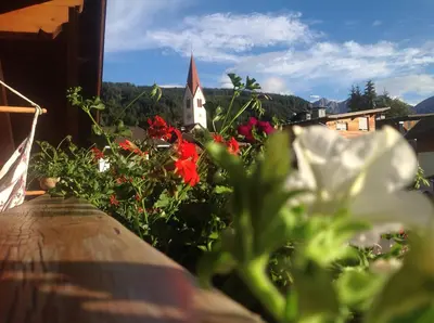 a garden with red flowers and a church in the background at Bio.top.Appartement in Rasun di Sopra