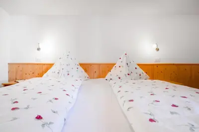 a bed with white sheets and red flowers on it at Appartements Beikircher in Valdaora