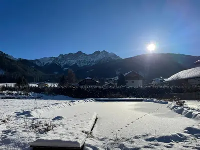 a snow covered yard with the sun shining on a mountain at App Unterhoezlhof in Valdaora