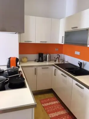 a small kitchen with white cabinets and an orange wall at Nel Cuore Verde di Bolzano in Bolzano