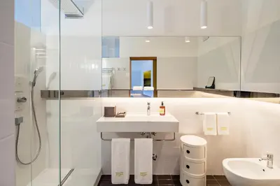 a white bathroom with a sink and a shower at Seehotel Ambach in Caldaro