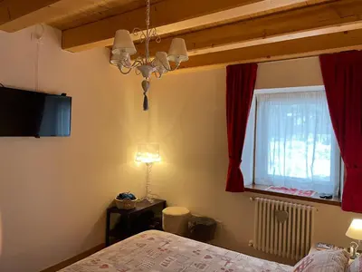 a bedroom with a bed and a chandelier and a window at Casa Romeo in San Vito di Cadore