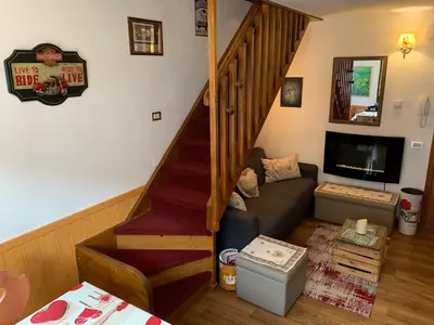 a living room with a staircase with a couch and a television at Appartamento Esprit Des Alpes in Canazei
