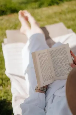 a person laying on a blanket reading a book at Villa Maier B&B & Apartments in Soprabolzano