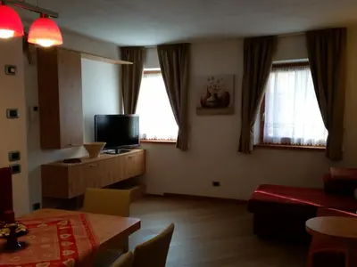 a living room with a table and a tv and two windows at Casa Alice 5.5 in Fiera di Primiero