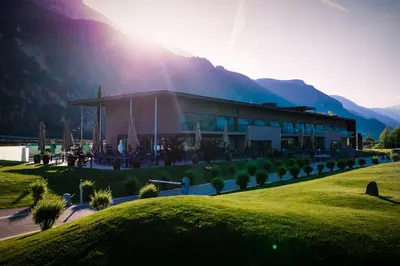 a building with the sun setting behind a mountain at The Lodge Sporthotel - Golfclub Eppan in Appiano sulla Strada del Vino
