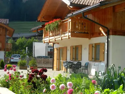 a house with a balcony and flowers in the yard at Anna Apartment in Pozza di Fassa