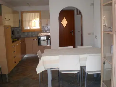 a kitchen with a table and some white chairs at Anna Apartment in Pozza di Fassa