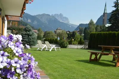 a group of chairs sitting on a lawn with mountains in the background at Anna Apartment in Pozza di Fassa