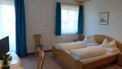 a bedroom with two beds with blue curtains and a table at Pension Runer in Terlano
