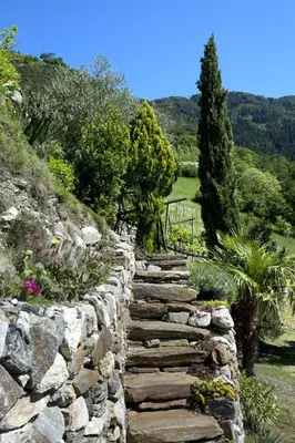 a stone path in a garden with flowers and trees at Biohof Niedereben in Rablà