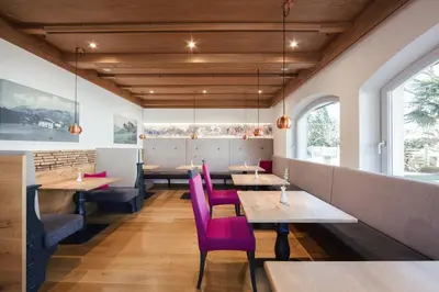 a restaurant with wooden ceilings and pink chairs and tables at Hotel Garni Sirmian in Merano