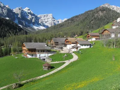 a village in the mountains with a green field at Agriturismo Lüch de Vanc in San Martino in Badia